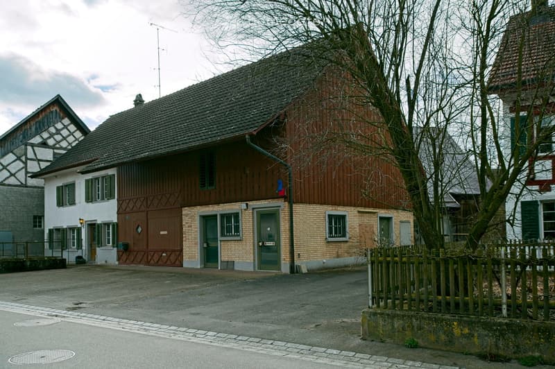 Two-story building with a mix of wooden and brick facades, multiple windows, and a wooden garage door.