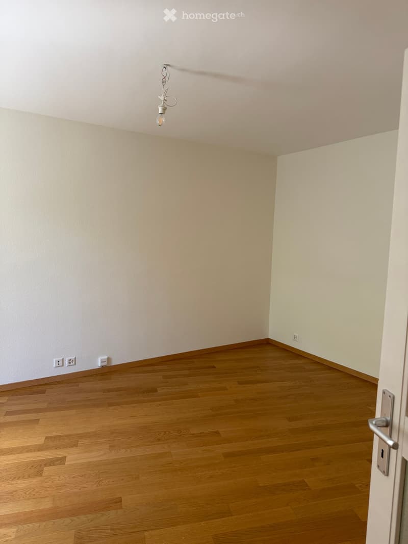 Empty room with wooden flooring, white walls, and a single hanging light fixture.