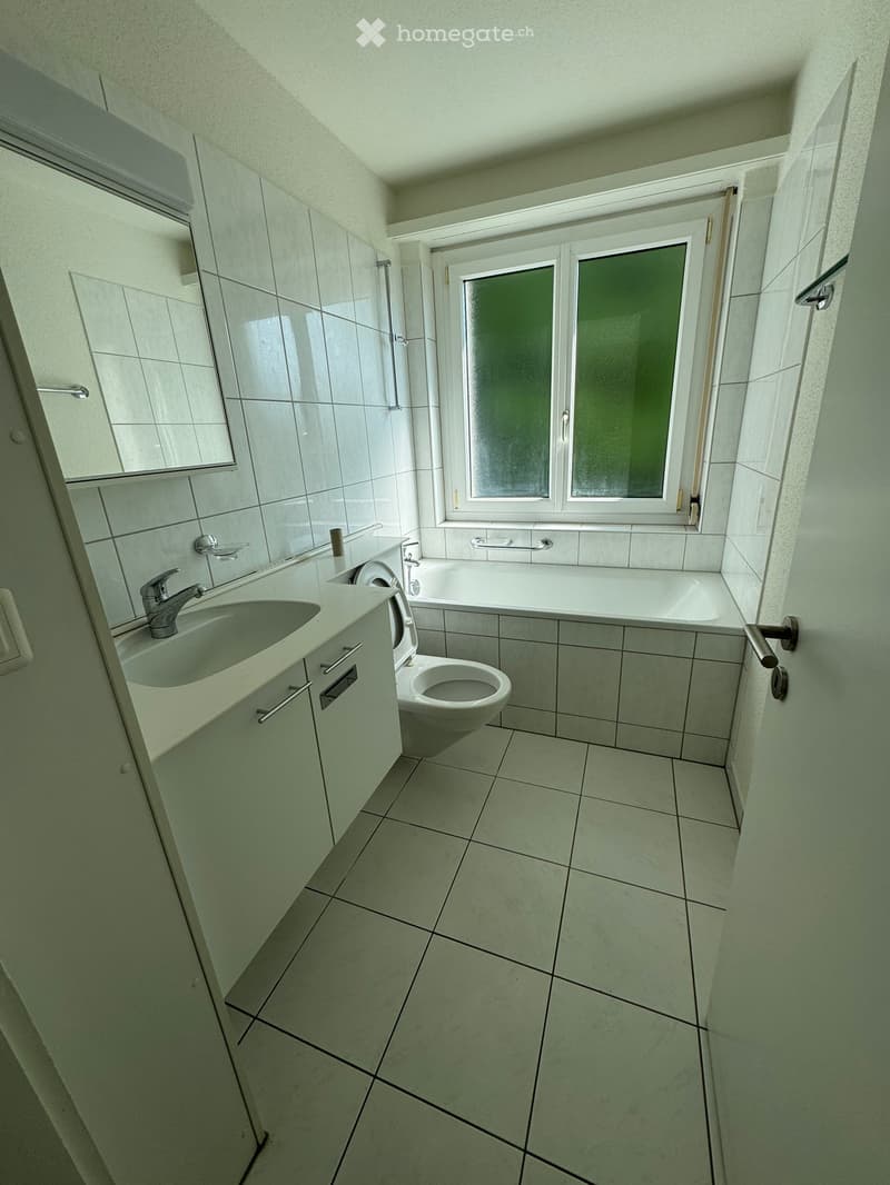 Bathroom. Modern bathroom with white tiles, a sink with a faucet, a toilet, a bathtub, and a window with frosted glass. The room features a cabinet with a mirror above the sink.