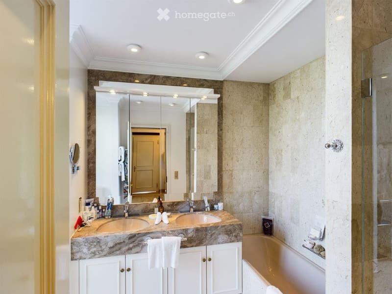 Elegant bathroom with double sinks, a large mirrored vanity, marble countertops, and a bathtub with a glass shower enclosure.