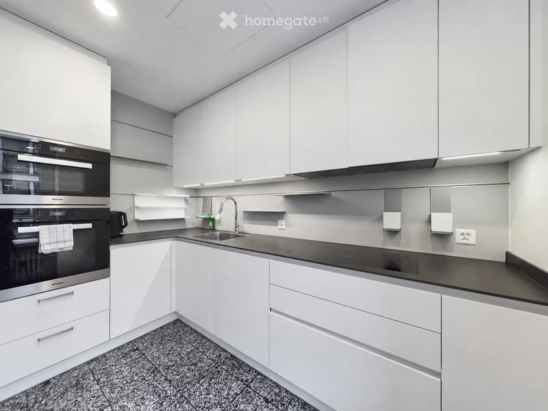 Modern kitchen with white cabinets, black countertop, stainless steel oven, sink, and faucet.