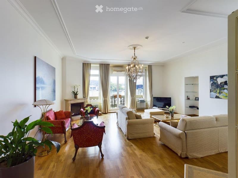 Elegant living room with wooden flooring, large windows offering a view, a fireplace, a chandelier, a sofa, armchairs, coffee table, and decorative plants.