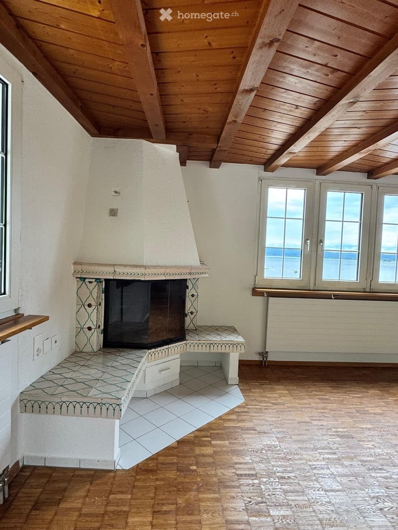 Room with wooden slanted ceiling, fireplace with decorative tiles, bench seating, large windows with ocean view.