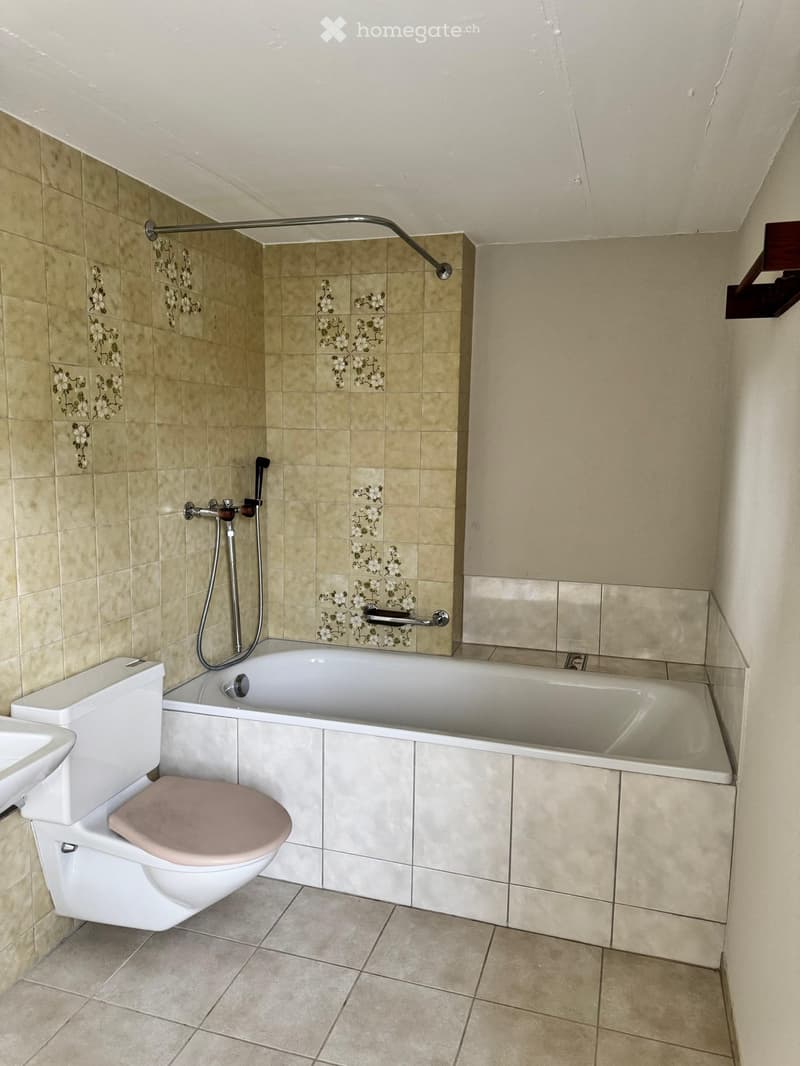 Bathroom with beige tiles, a bathtub with a handheld shower, a toilet, and a sink.