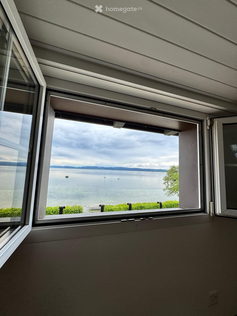 A large window with a view of a body of water, boats, and distant hills under a cloudy sky.