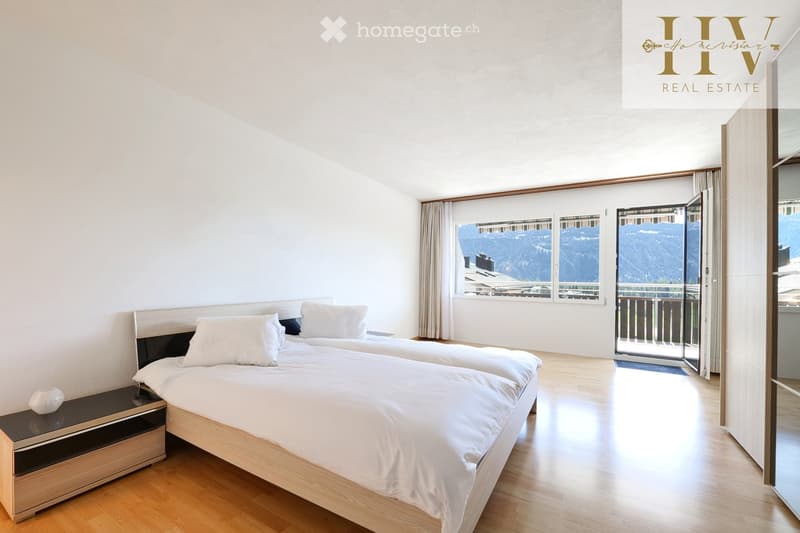 Bright bedroom with two single beds, nightstand, large windows with mountain view, and sliding glass door leading to a balcony.