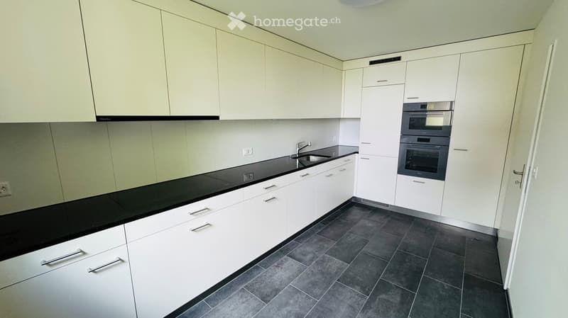 Modern kitchen with white cabinets, black countertops, and stainless steel appliances including a sink and oven.