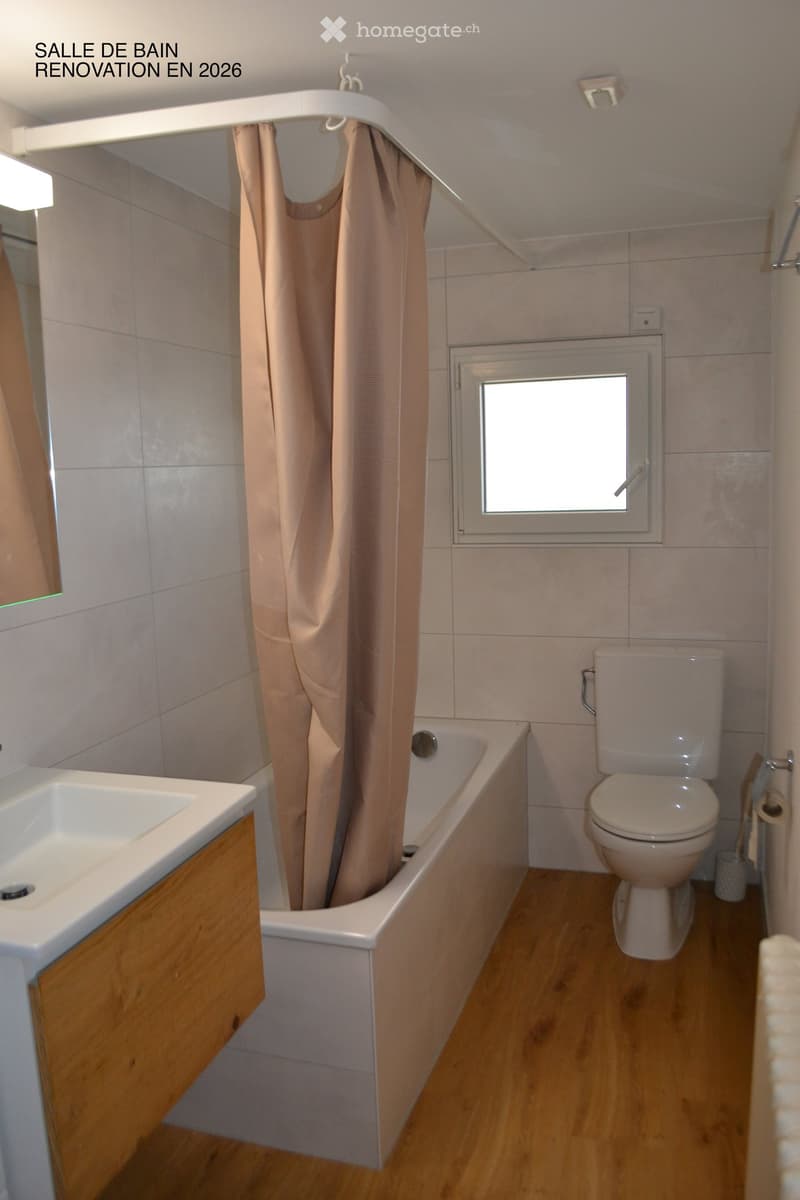 Modern bathroom with a bathtub, toilet, sink, and a window. Features a wooden floor, tiled walls, and a beige shower curtain.