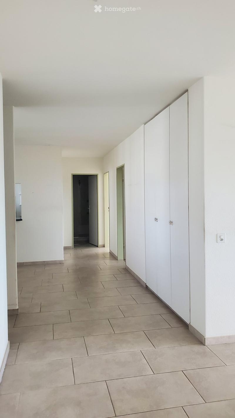 Empty hallway with tiled floor, white walls, and built-in white cabinets on one side. Three doors lead to other rooms.