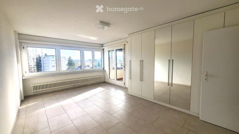 Empty room with tiled floor, large windows, built-in wardrobes, and a radiator under the windows.