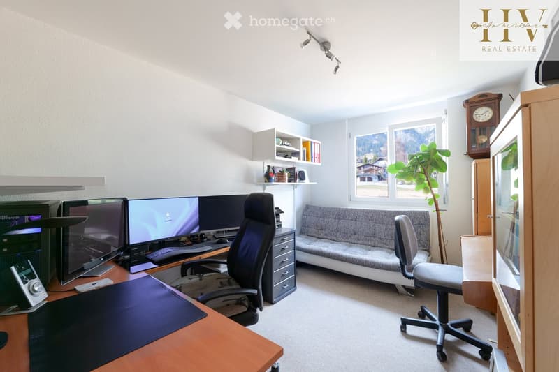 A well-lit, modern office space with a large desk, multiple computer screens, ergonomic chair, sofa, and decorative shelves. Large windows offer a scenic view.