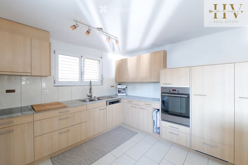 Modern kitchen with light wooden cabinets, granite countertops, stainless steel appliances, and a window above the sink.
