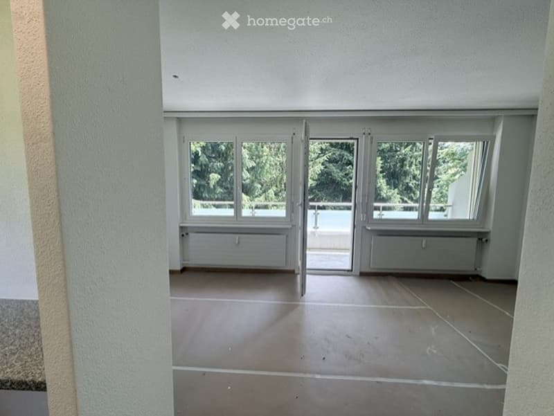 Empty room with large windows and a sliding door leading to a balcony. Light-colored tiled floor and white walls.