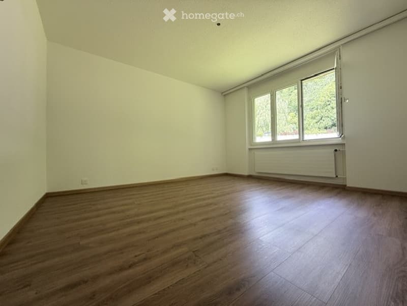Empty room with wooden flooring, white walls, and large windows allowing natural light.