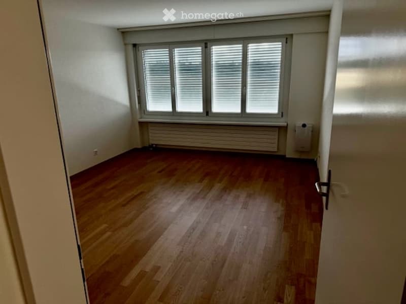 Empty room with wooden flooring, white walls, and large window with blinds. No furniture or equipment present.