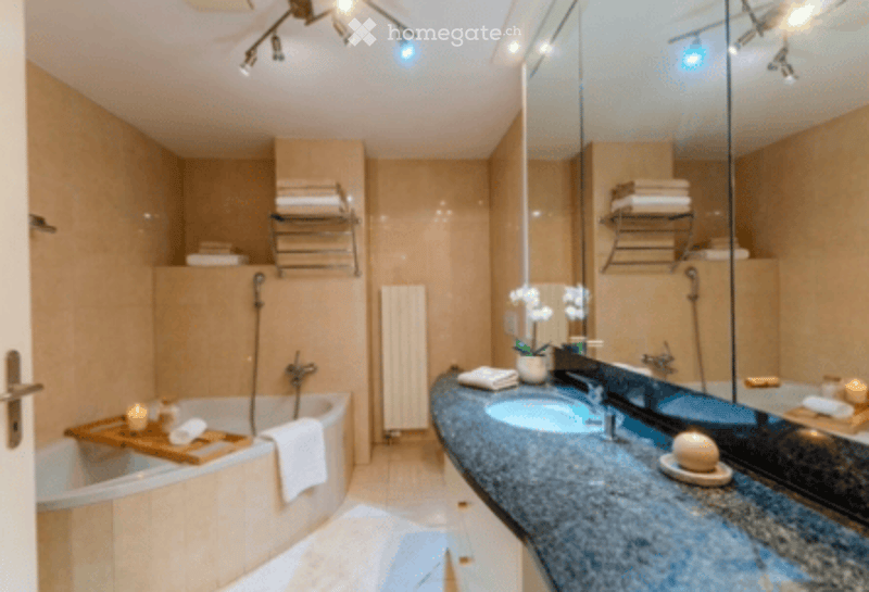 Modern bathroom with a bathtub, double sink, large mirror, towel rack, and decorative elements like a flower vase and candle.