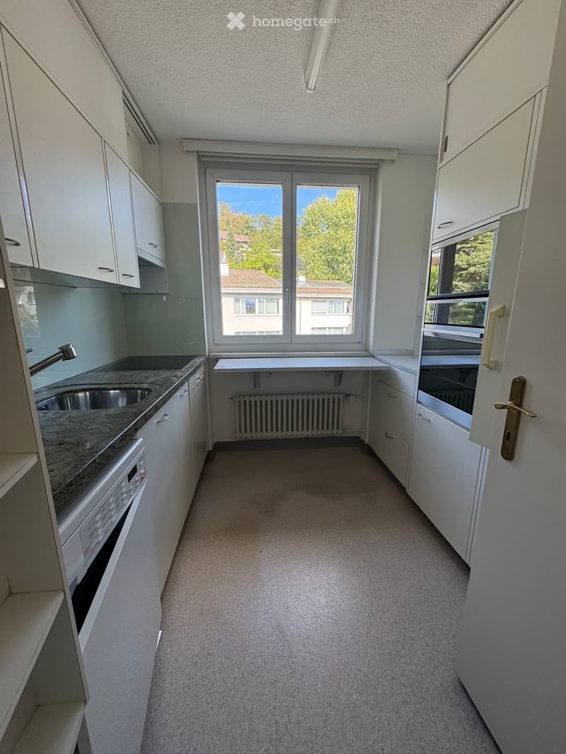 Empty kitchen with white cabinets, granite countertop, sink, and a window overlooking a residential area.