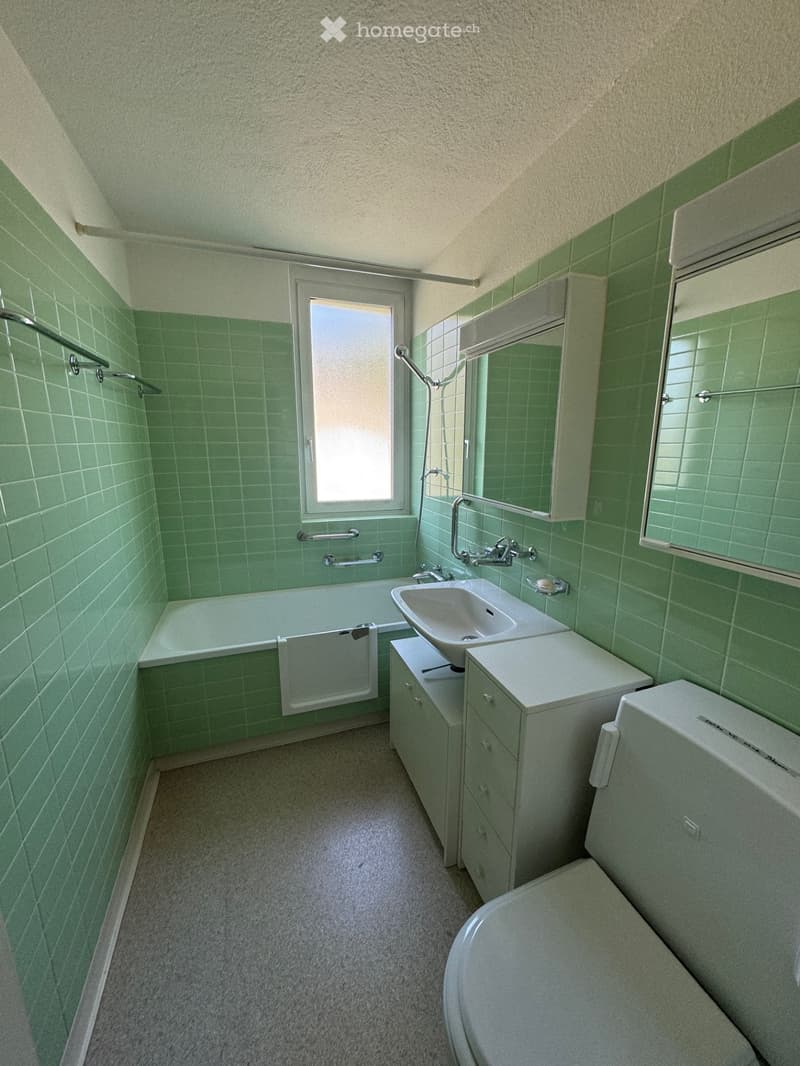 Bathroom with green tiled walls, bathtub, sink, toilet, and built-in cabinetry. Features a window and towel rack.