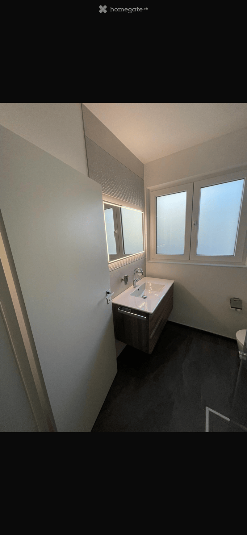 Modern bathroom with a white sink, chrome faucet, mirrored cabinet, and dark tiled floor.