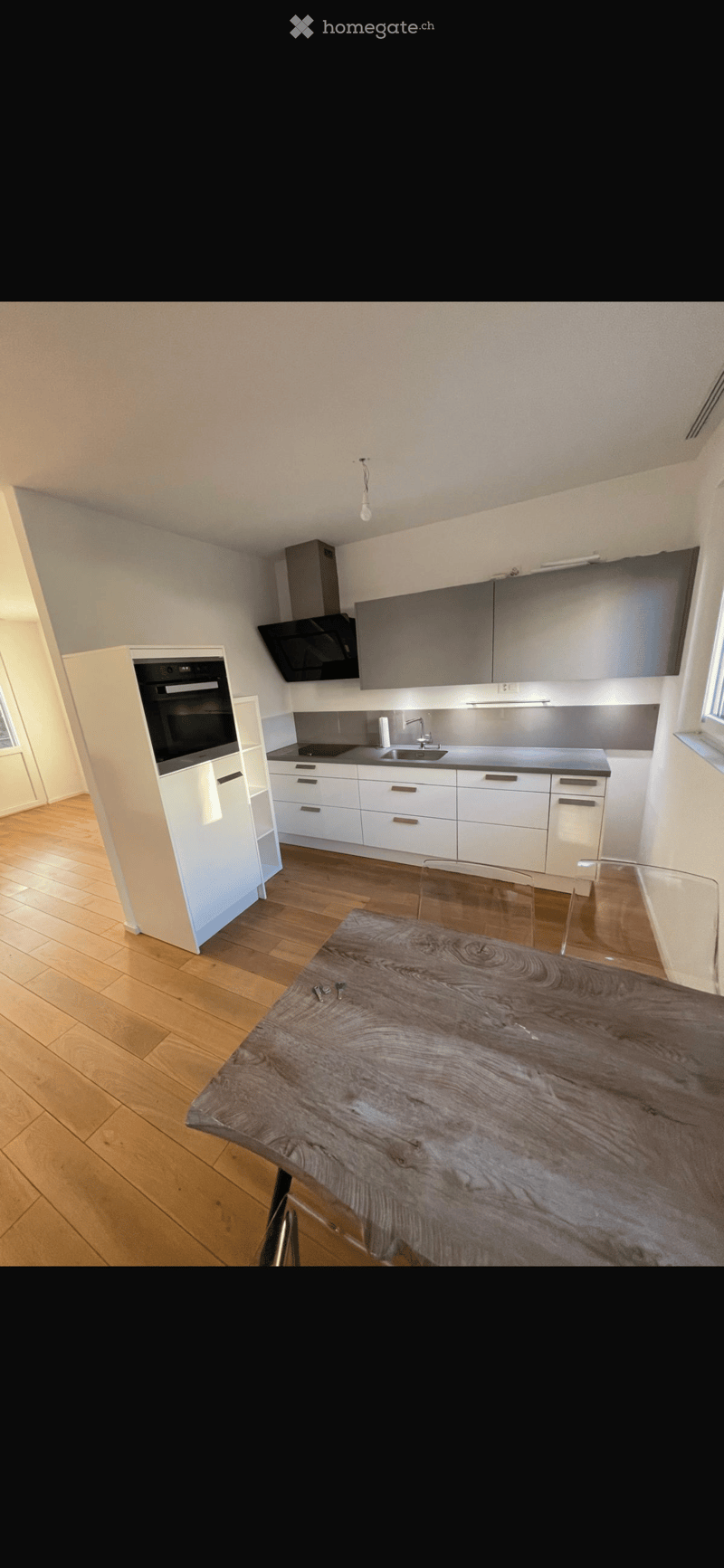 Modern kitchen with white cabinets, stainless steel appliances, wooden floor, and a wooden dining table with glass chairs.