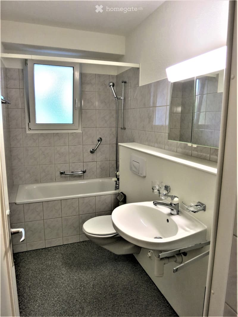Bathroom with a toilet, sink, bathtub, and mirror. Features tiled walls and a window above the bathtub.