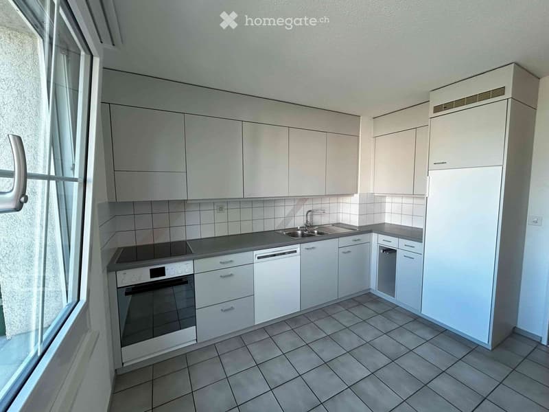 Modern kitchen with white cabinets, tiled walls, and grey countertops. Features an oven, dishwasher, and sink.