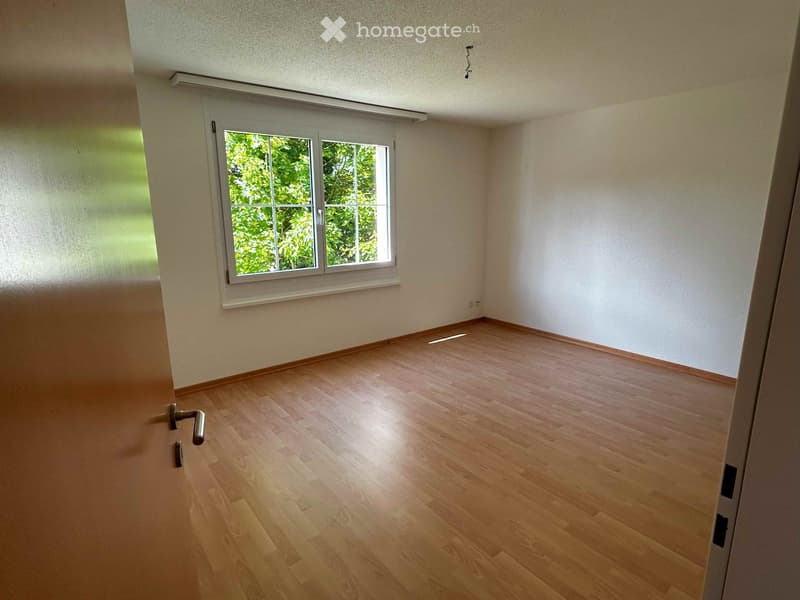 Empty room with wooden flooring, white walls, and a window with white frame showing greenery outside.