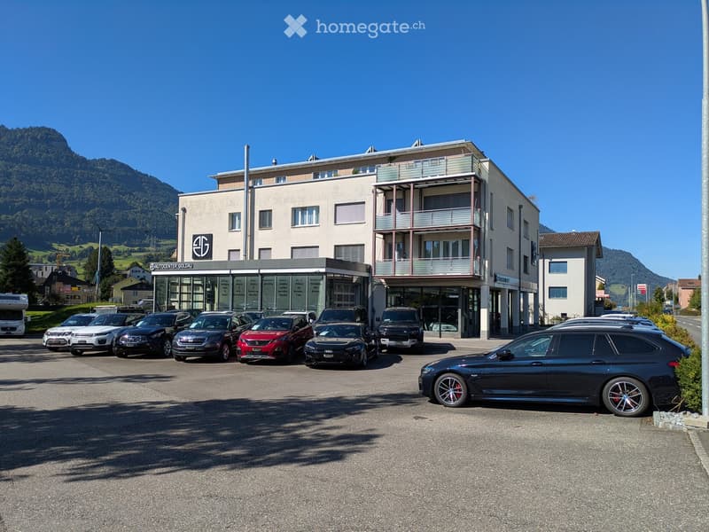 3 story building with many windows, balcony, outdoor parking lot, surrounded by mountains
