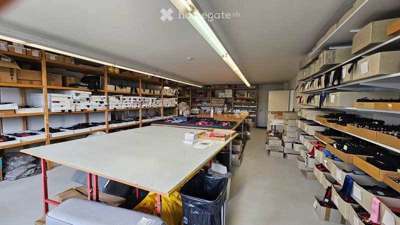 Furnished Room. A spacious storage or workshop area with large tables, shelves filled with boxes and items, and organized storage units.