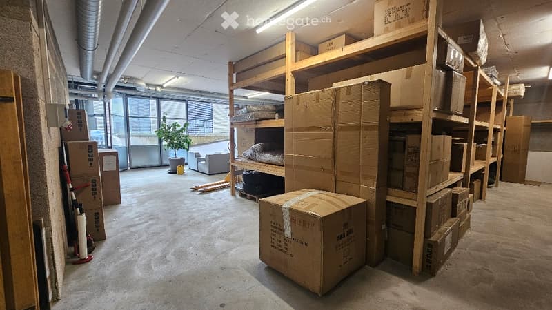 Unfurnished Room. Empty room with exposed concrete floors, large windows, and wooden shelving units filled with cardboard boxes. No furniture or equipment is present.