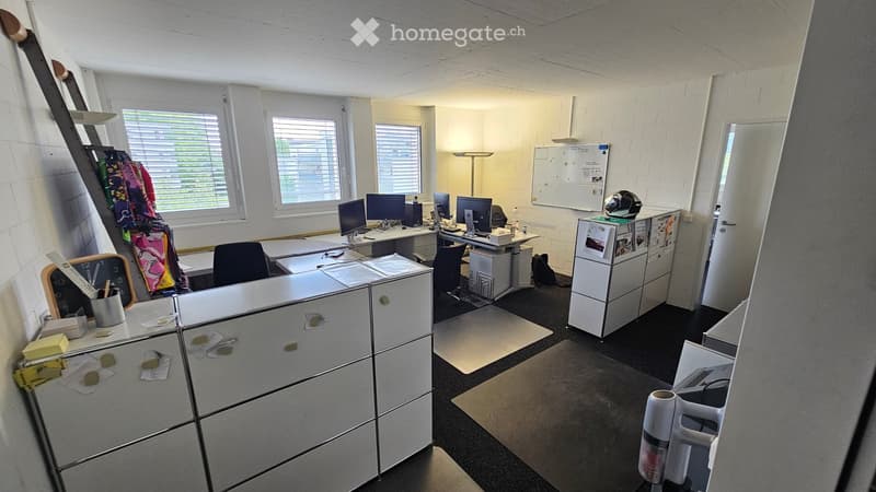 Furnished Room. Office space with desks, chairs, computers, filing cabinets, and a whiteboard. The room has large windows with blinds and is well-lit.