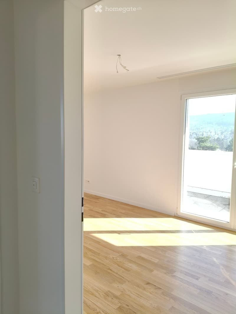 Empty room with light wooden flooring, white walls, and a large window offering a scenic view.