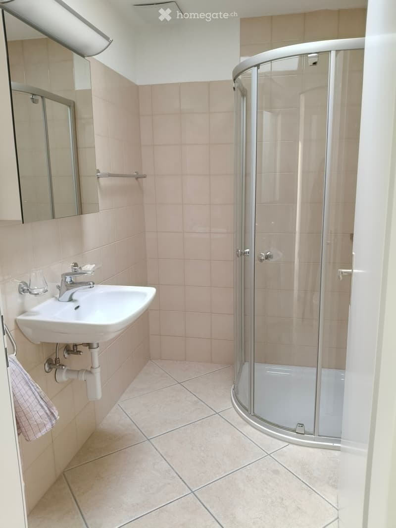 Modern bathroom with beige tiles, a white sink, a glass-enclosed shower, and a towel hanging on a rack.