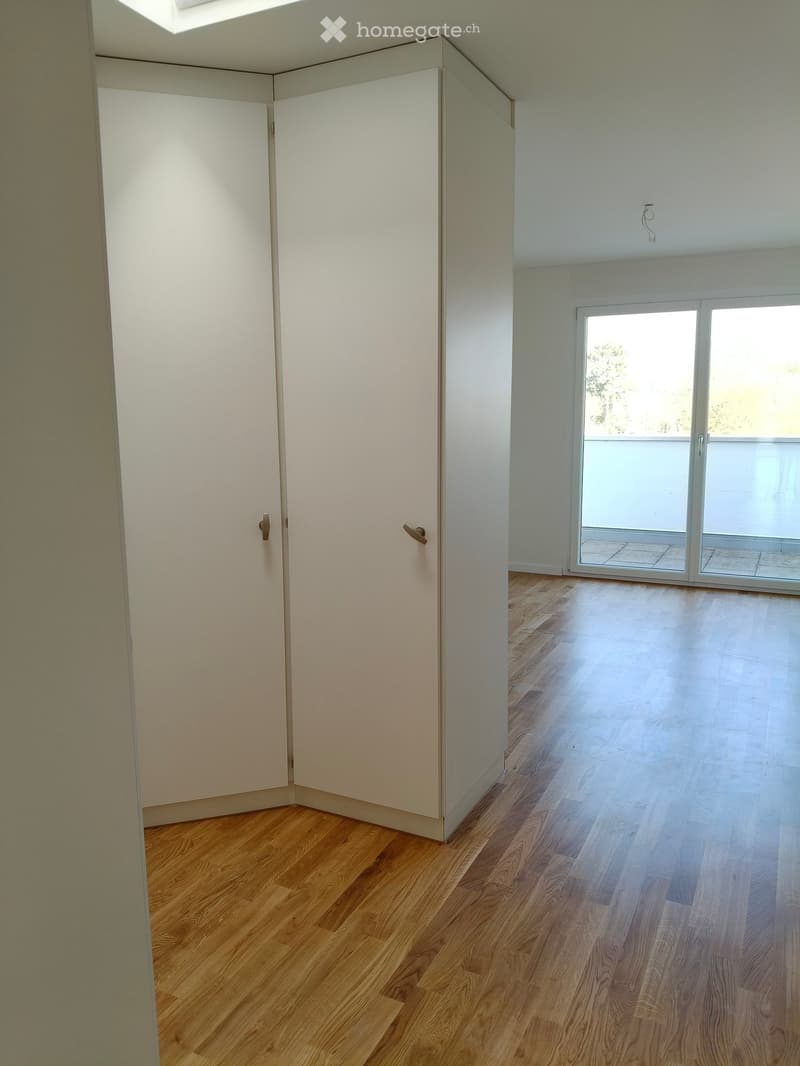 Empty room with wooden flooring, white walls, and a sliding glass door leading to a balcony.