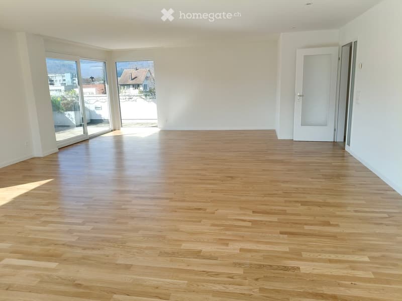 Empty room with light wooden flooring, white walls, large sliding glass doors, and a white door.