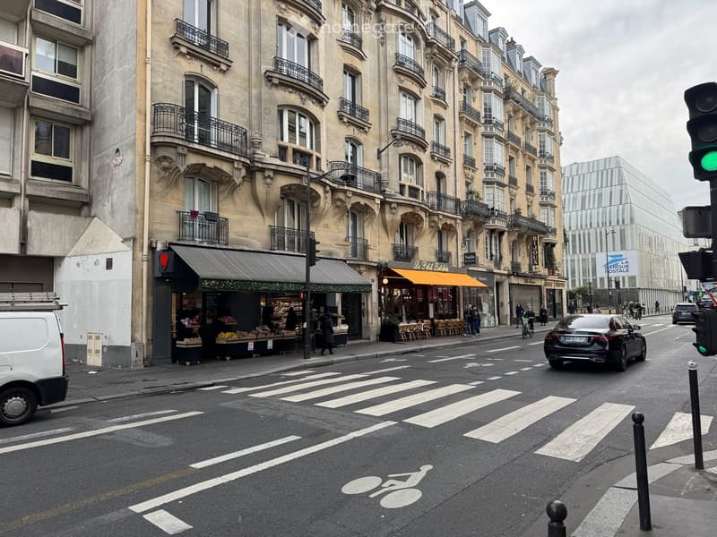 A building with multiple floors and a store front, a road with cars and a crosswalk, a traffic light.