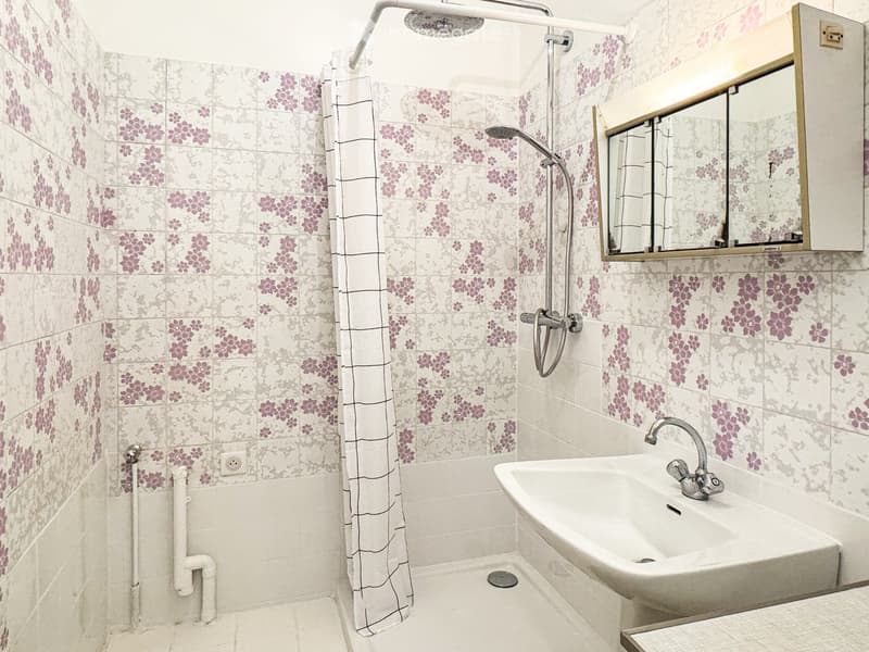 Bathroom with shower, sink, floral wallpaper, mirror, power outlet
