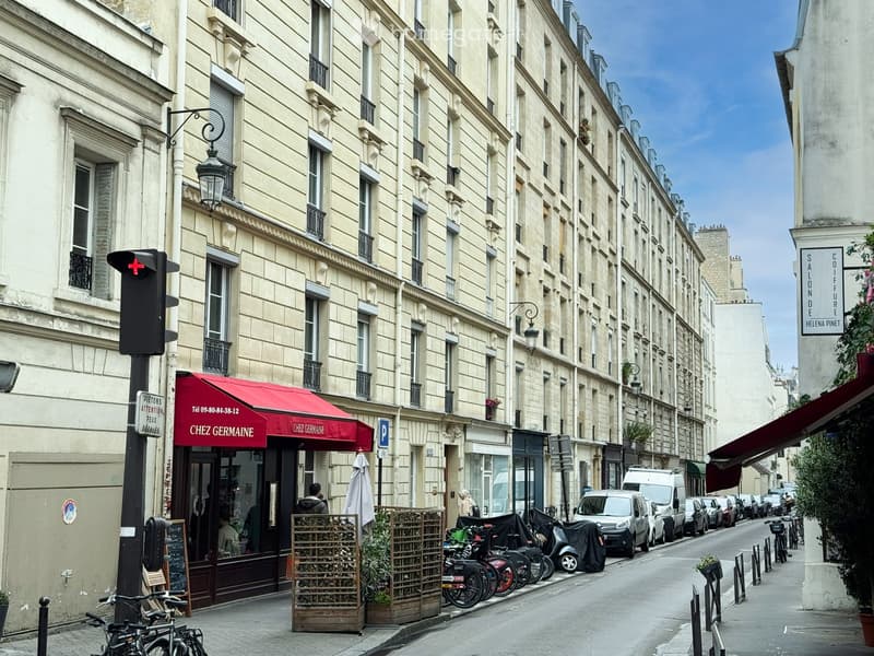 4 story building, beige painted, multiple windows, red awning, parked cars, bicycles, plants