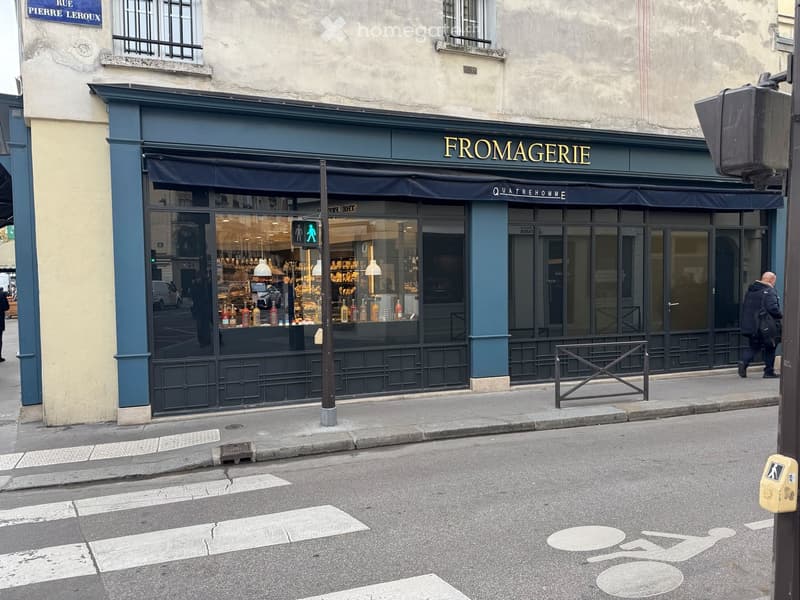 Storefront of a store named Fromagerie located on Rue Pierre Leroux with glass windows and black awning, with a person walking on the sidewalk in front