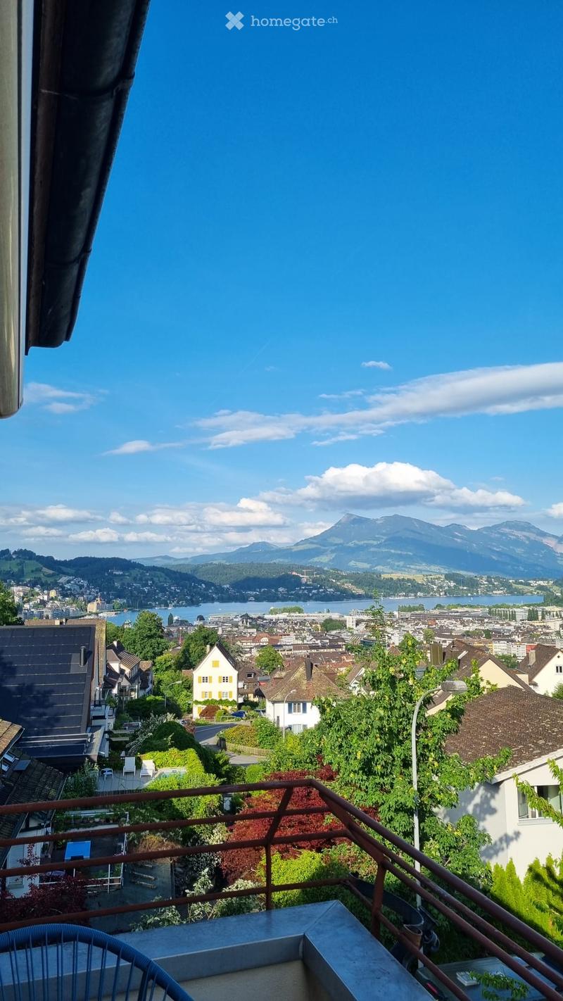 Balcony with a scenic view of a cityscape, lake, and mountains in the background.