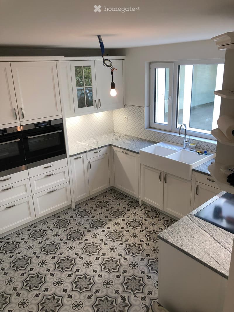Modern kitchen with white cabinets, stainless steel oven, large sink, and patterned tile floor.