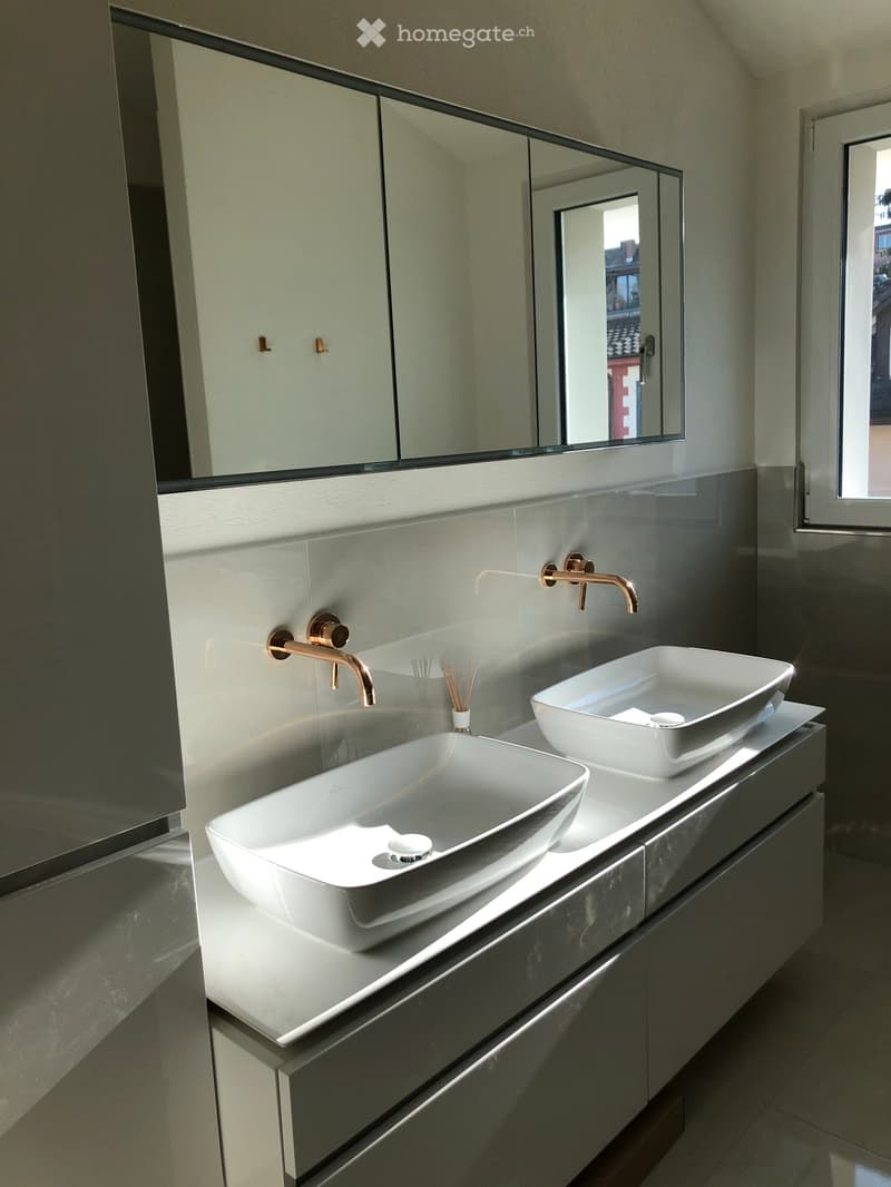 Modern bathroom with two white sinks, gold faucets, a large mirror, and built-in cabinets.