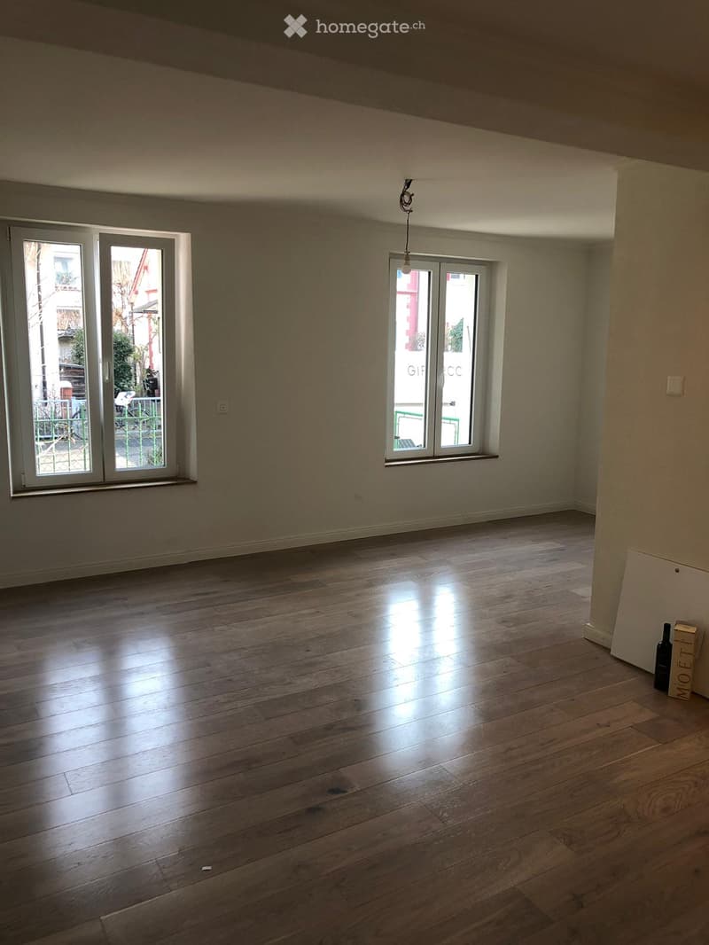 Empty room with wooden flooring, large windows, and neutral-colored walls.