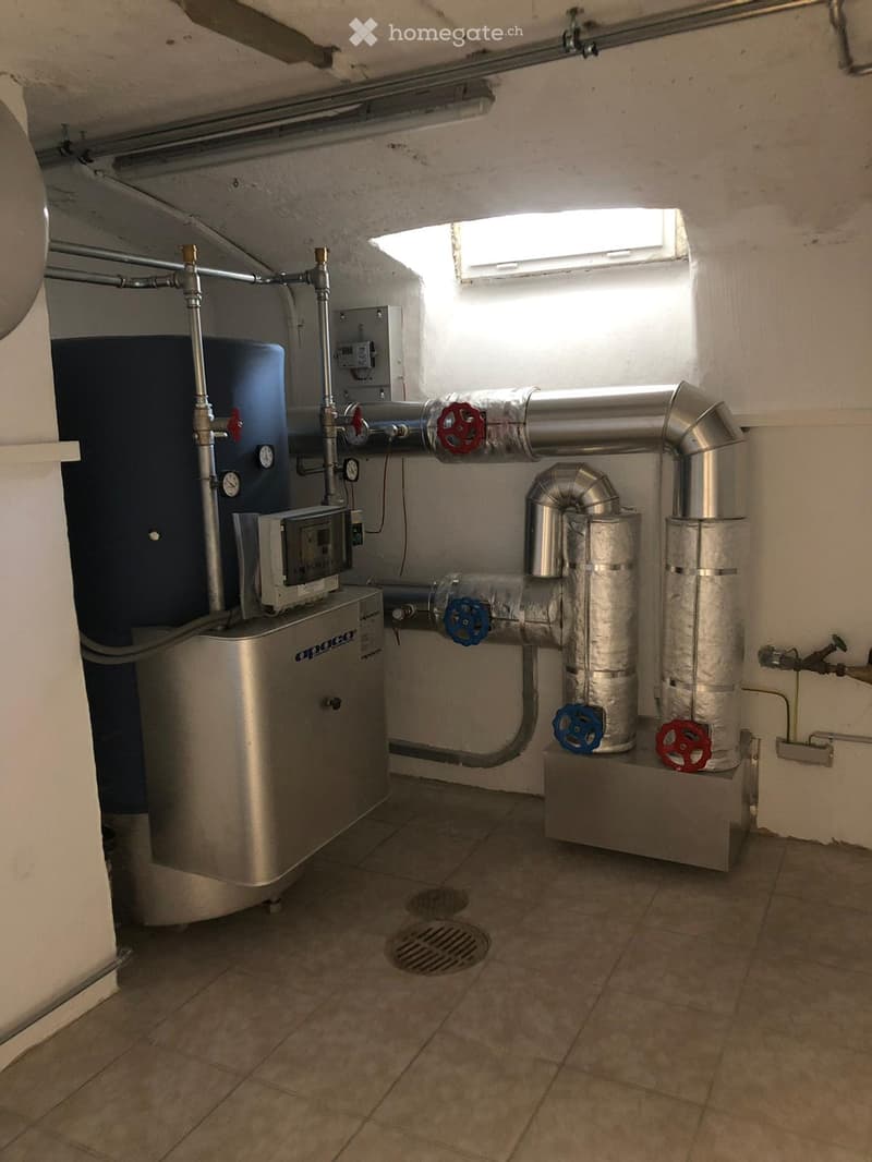 Utility room with water heater, pipes, valves, and control panel.