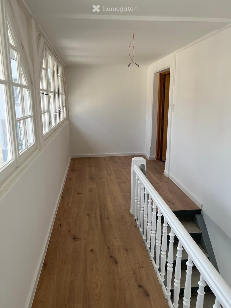 Hallway with hardwood floor, white railings, large windows, staircase to upper floor