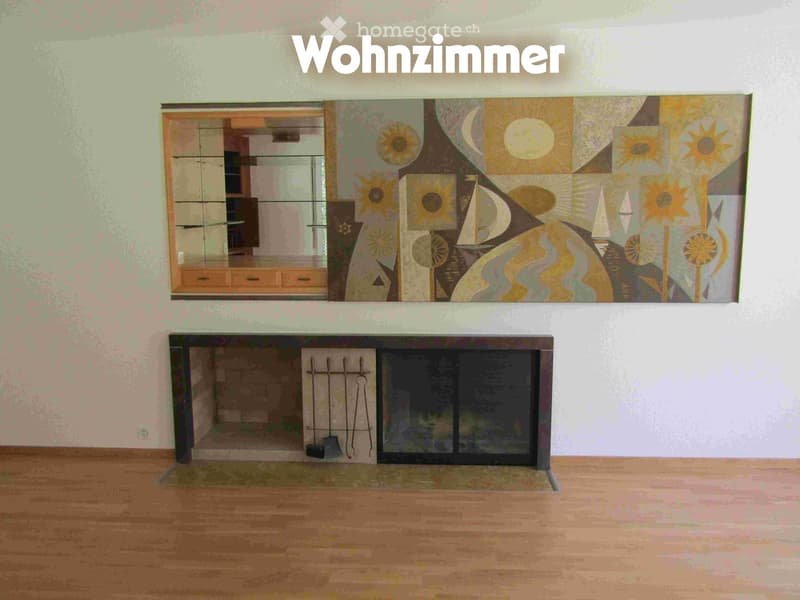 Empty room with wooden flooring, a fireplace, and a large abstract painting on the wall. A mirror and cabinet are visible in the background.