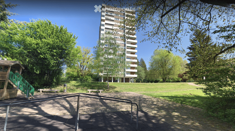A park area with a playground, benches, and a multi-story residential building in the background.