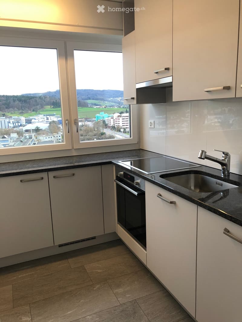 Modern kitchen with white cabinets, dark countertops, stainless steel sink, and built-in oven and microwave. Large windows offer a scenic view.