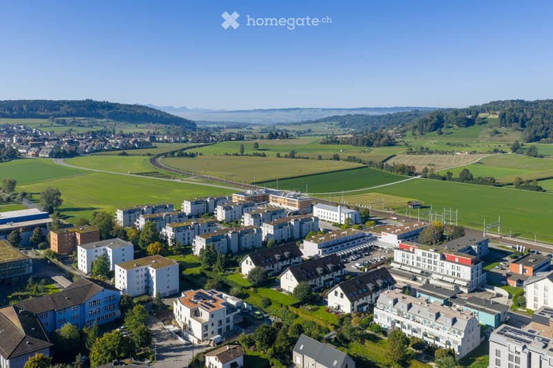 Aerial view of a residential area with multiple apartment buildings, parking lots, and surrounding green fields and forests.