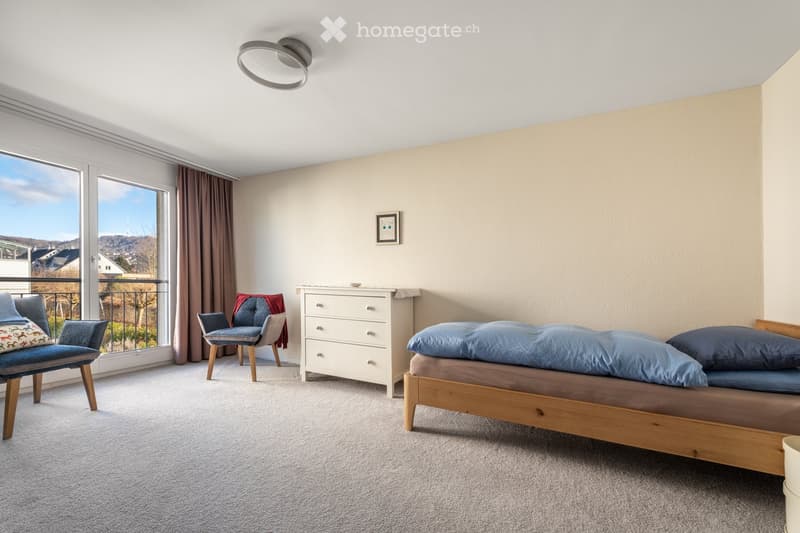 Bright bedroom with a wooden bed, two chairs, a dresser, and a large window offering a scenic view.